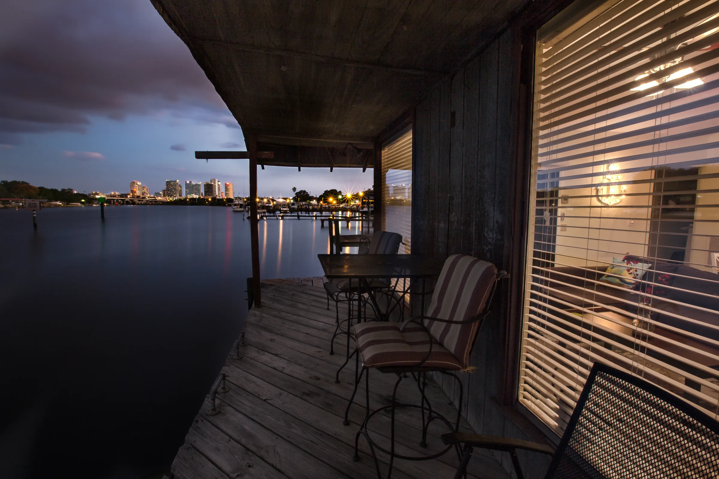 Covered dock porch at dusk with bistro chairs and city lights across water