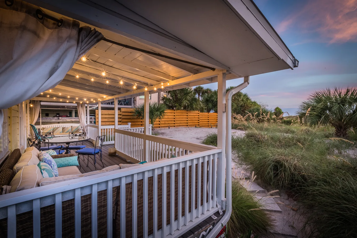 Canopied deck with string lights and seating beside grassy dunes